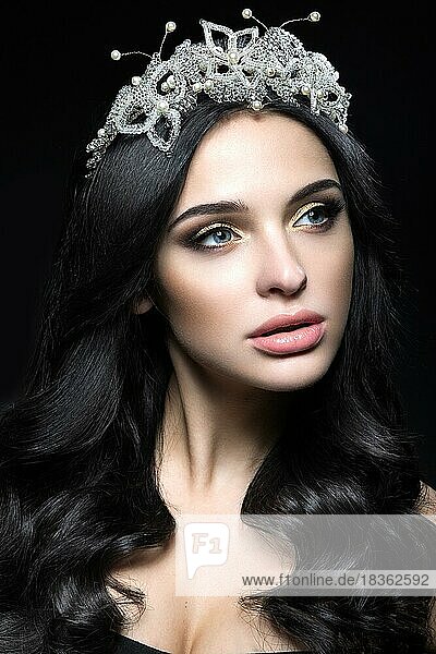 Schöne dunkelhaarige Frau mit einer Krone aus Edelsteinen  Locken und Abend-Make-up. Schönes Gesicht. Bild im Studio auf einem schwarzen Hintergrund aufgenommen