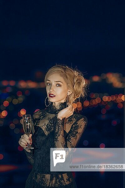 Schönes Mädchen mit Glas Champagner stehen in der Nähe des Fensters mit unscharfen Nacht Stadt auf Hintergrund