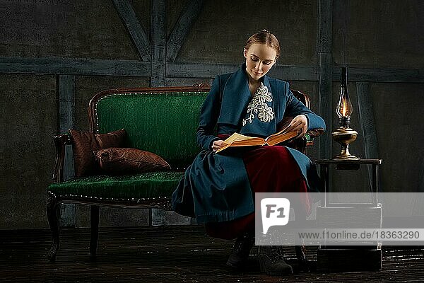 Attraktive Dame in altmodischer Kleidung liest altes Buch in der Nähe von Vintage Kerosinlampe