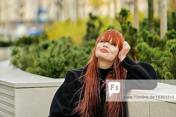 Dreamy young redheaded woman sitting on bench