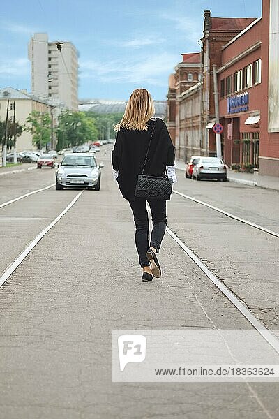 Rückenansicht eines Hipster-Mädchens in schwarzem Poncho und Jeans  das in der Mitte der Straße läuft