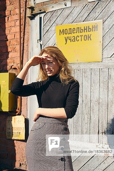 Attraktives Mädchen in der Nähe der Fabriktür mit Warnschildern  die die Augen mit der Hand bedecken. (Inschrift auf Platte ist auf Russisch kann als Modell Bereich übersetzt werden und nicht betreten)