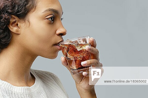 Closeup Porträt der jungen afrikanisch-amerikanischen Frau trinken Cola mit Eis über grauen Hintergrund