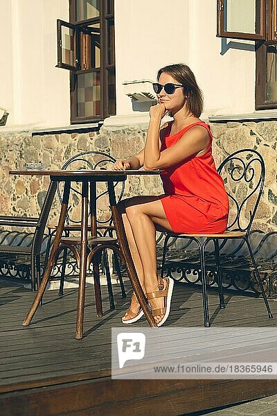 Mädchen mit Sonnenbrille sitzt an einem Tisch auf der Terrasse eines Cafés in sonnigen Tag