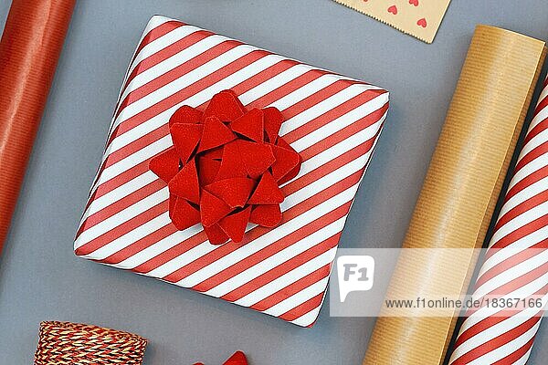 Flat Lay Konzept für Weihnachten Geschenkverpackung mit schönen roten und weißen gestreiften Geschenk-Box mit großen roten Bogen  und natürliche Geschenkpapier auf grauem Hintergrund