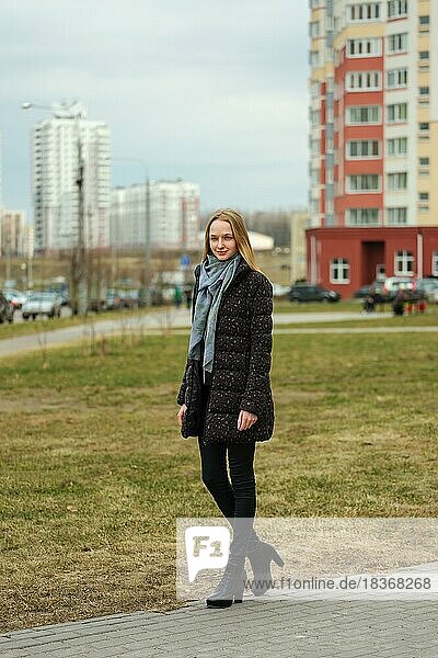 Happy girl in jeans and down jacket walking along the street in residential area with high houses