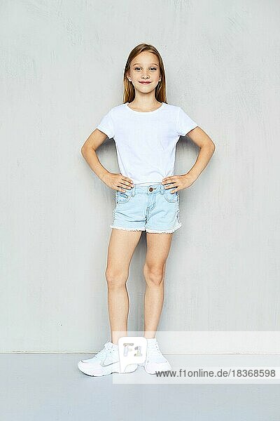 Junges sportliches Mädchen in weißem T-Shirt und Jeansshorts posiert im Studio