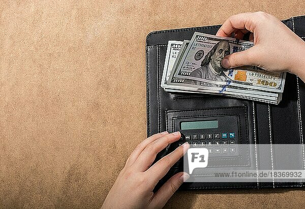 Hand hält amerikanische Dollarnoten neben einem Taschenrechner