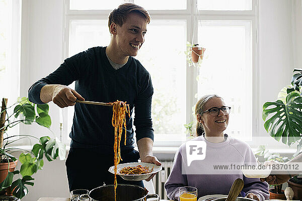 Lächelnder Mann beim Entfernen von Spaghetti in einem Teller zu Hause