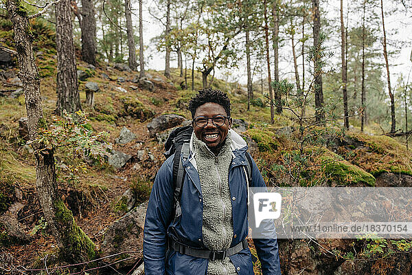 Happy mature man with backpack standing in forest during vacation