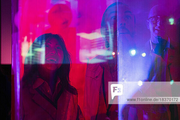 Glückliche männliche und weibliche Geschäftskollegen  gesehen durch Glas in einem beleuchteten Ausstellungszentrum