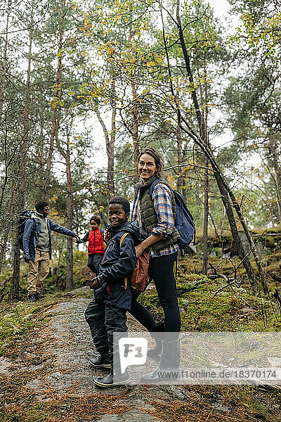 Side view of smiling woman standing on trail with son in forest during vacation
