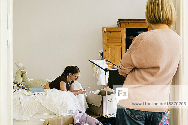 Rear view of parent looking at daughter using smart phone lying on bed at home