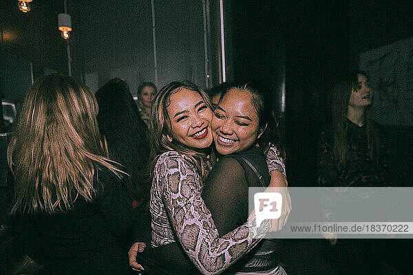Porträt von fröhlichen jungen Frauen  die sich umarmen  während sie sich in einem Nachtclub vergnügen