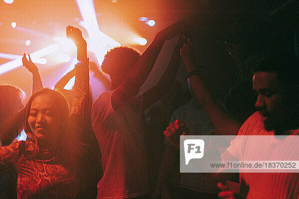 Glückliche junge männliche und weibliche Freunde genießen den Tanz in einem beleuchteten roten Nachtclub