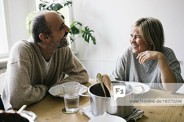 Happy mature couple talking to each other sitting at dining table in home