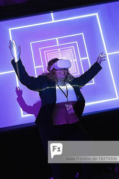 Glückliche Geschäftsfrau mit VR-Brille  die mit erhobenen Armen im Kongresszentrum steht