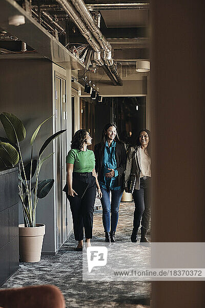 Smiling multiracial businesswomen discussing while walking in office