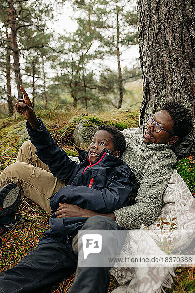 Junge zeigt auf einen Baum im Wald  während er sich mit seinem Vater hinlegt