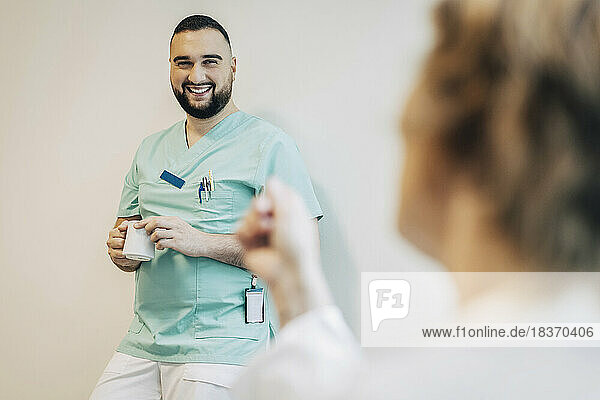 Glückliches männliches Krankenhauspersonal mit Kaffeetasse an eine weiße Wand gelehnt