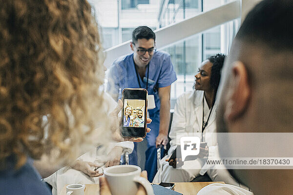 Weibliche Krankenschwester  die während einer Kaffeepause im Krankenhaus ein Selfie mit einem Kollegen per Smartphone macht