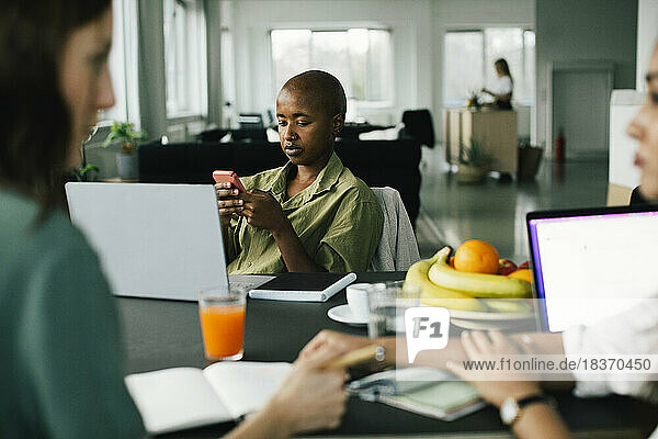 Geschäftsfrau mit rasiertem Kopf  die im Büro sitzend ein Smartphone benutzt