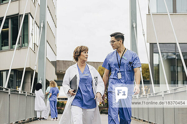 Male healthcare worker talking with female physician while walking on bridge