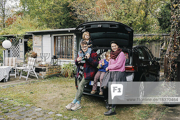 Happy parents with daughters near electric car parked outside house