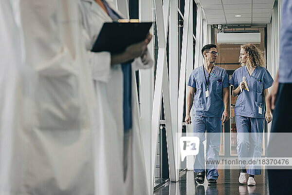 Nurse having banana talking with colleague while walking in corridor of hospital