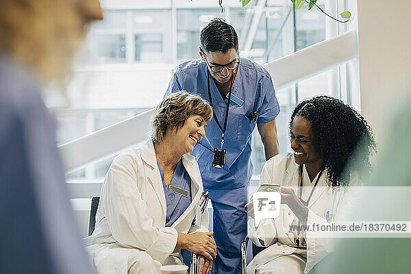 Happy mature female doctor sharing smart phone with coworkers during coffee break