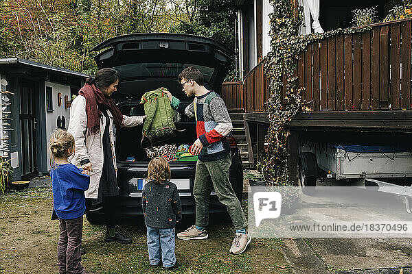 Familie bereitet sich auf ein Picknick vor  während sie Sachen in den Kofferraum eines Elektroautos lädt