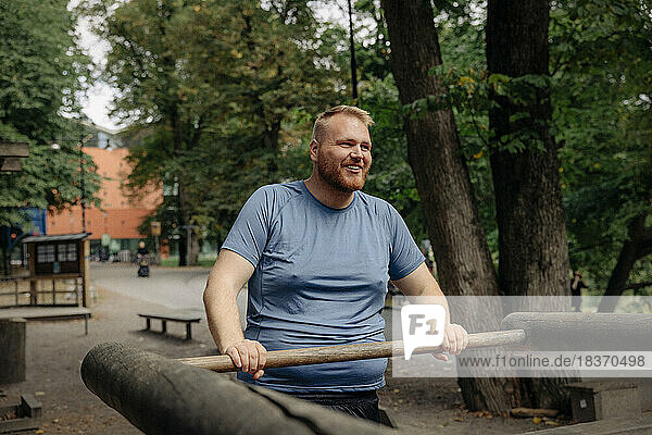 Smiling overweight man exercising while standing at park