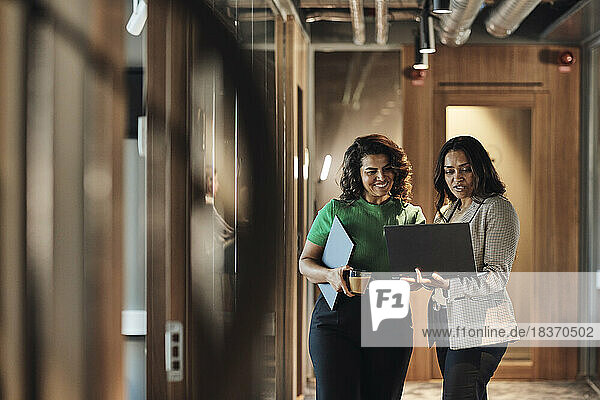 Mature female entrepreneurs discussing over laptop while standing in corridor at office
