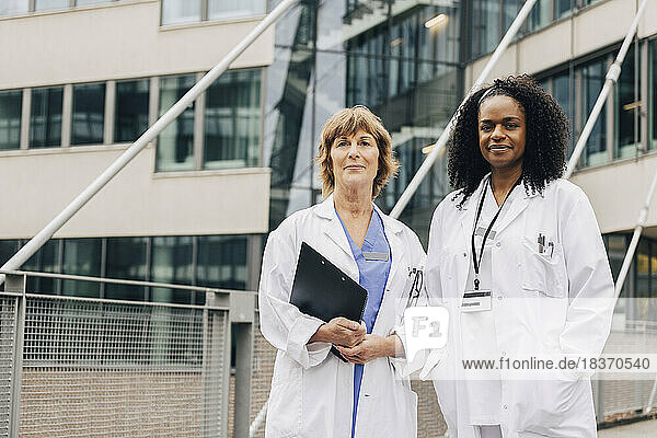 Portrait of confident multiracial female doctors standing in front of hospital