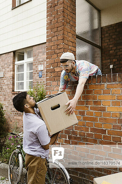 Mann reicht seinem Freund einen Karton  während er sich an eine Mauer lehnt
