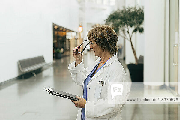 Side view of female doctor wearing eyeglasses while holding file at hospital