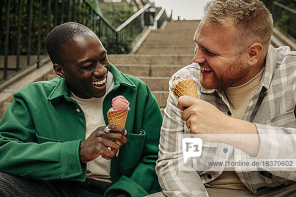 Happy multiracial male friends enjoying ice creams while sitting on steps
