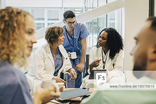 Ärztin mit Tablet-PC im Gespräch mit Kollegen während der Kaffeepause im Krankenhaus