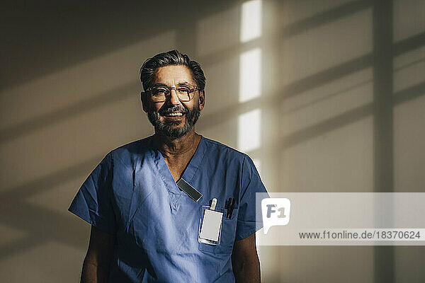 Porträt eines glücklichen männlichen Arztes  der in einem Krankenhaus an der Wand steht