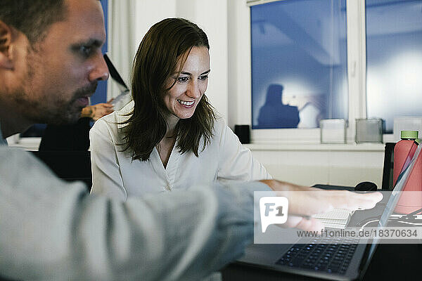Lächelnde Geschäftsfrau  die mit einem männlichen Kollegen im Büro am Laptop arbeitet