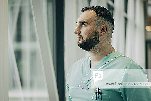 Thoughtful male nurse looking through window in hospital
