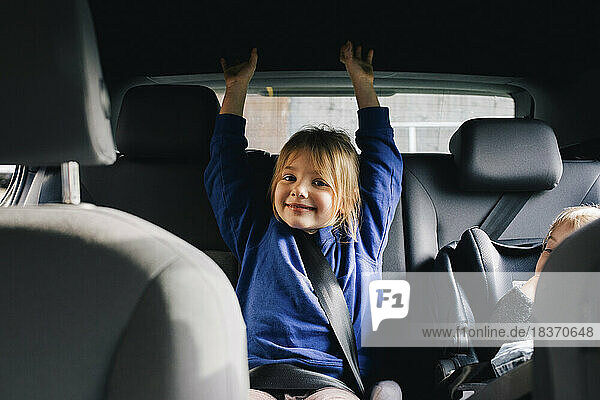 Porträt eines lächelnden Mädchens mit erhobenen Armen auf dem Rücksitz eines Autos
