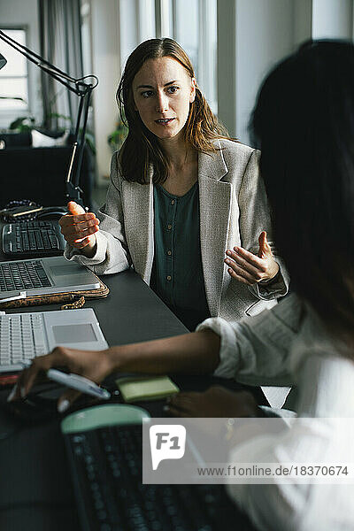 Geschäftsfrau gestikuliert beim Erklären einer Kollegin am Schreibtisch im Büro