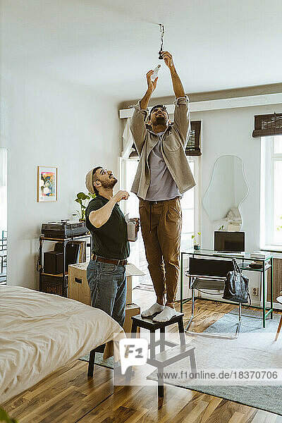 Mann installiert Glühbirne auf einem Hocker stehend bei seinem Freund zu Hause