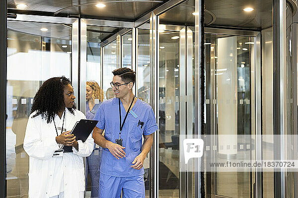 Male and female doctor talking while walking through revolving door