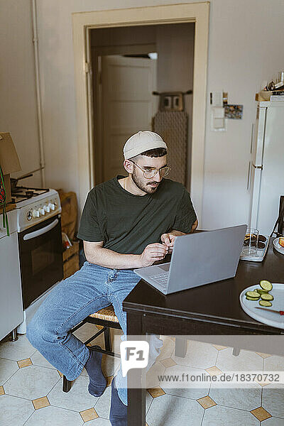 Mann mit Laptop am Esstisch in der Küche zu Hause sitzend