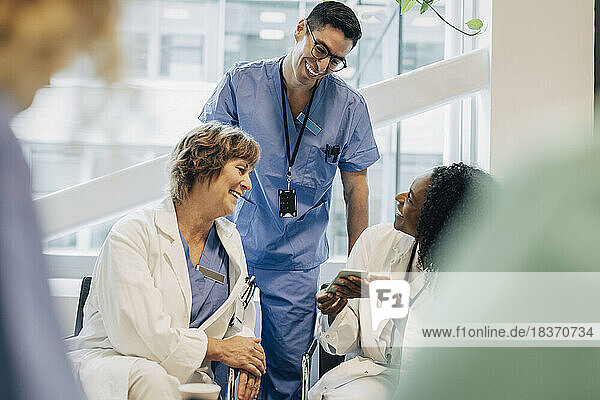 Lächelnde Ärztin teilt ihr Smartphone mit Kollegen während einer Pause im Krankenhaus