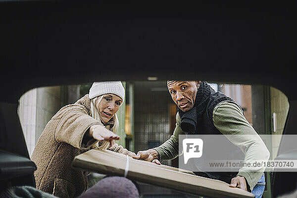 Reife Frau führt Mann beim Einladen von Karton in den Kofferraum eines Autos