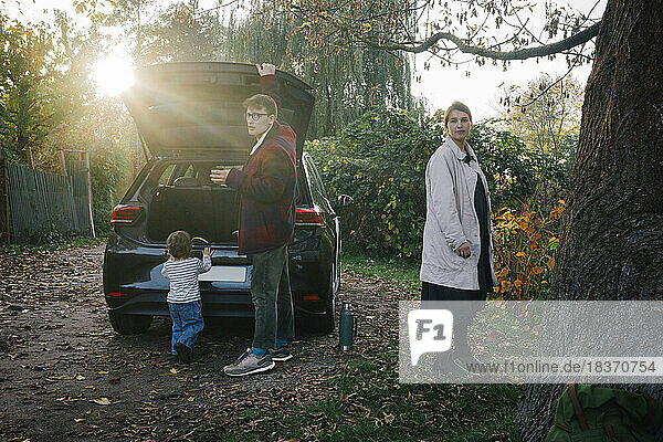 Vater und Mutter mit Tochter stehen an einem sonnigen Tag in der Nähe eines Elektroautos