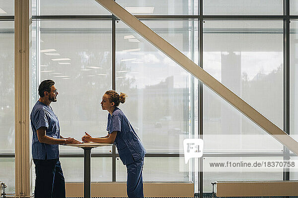 Side view of hospital staff discussing while standing by window in hospital